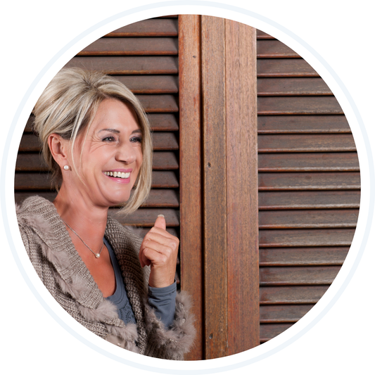 Blonde caucasian woman smiling wearing a brown sweater and blue long sleeved shirt